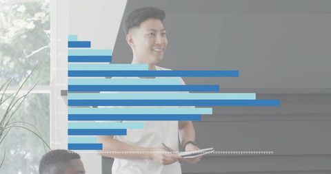 Asian presenter showing bar chart in bright office meeting smiling and taking notes