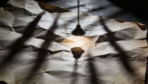 Pendant lamp casting warm light on crumpled parchment with dramatic chiaroscuro shadows