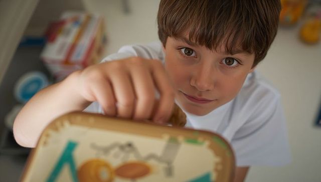 Preteen boy reaching into colorful metal lunchbox on pantry shelf