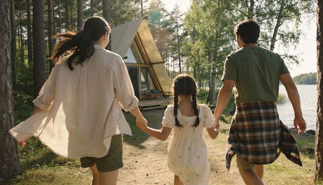 Family walking toward triangle lakeside cabin holding hands at golden hour