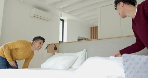 Friends having fun arranging pillows in modern minimalist bedroom