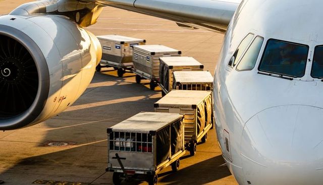 Commercial widebody jet at gate with turbofan and cargo dollies during golden hour operations