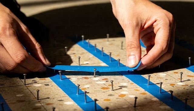 Hands applying blue painter tape on terrazzo tile grid for precise masking and layout