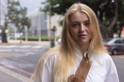 Blonde woman standing on overcast downtown sidewalk wearing white shirt and brown crossbody