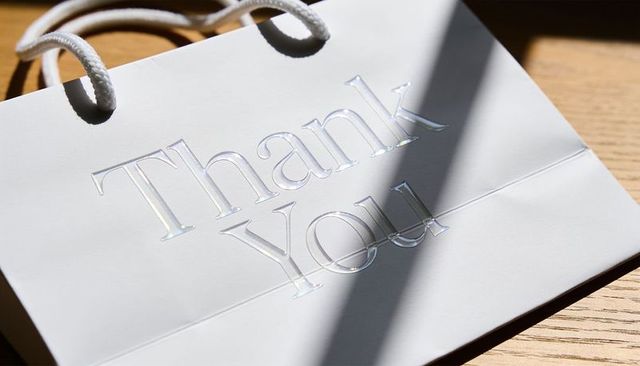 Sunlight casting diagonal shadow on white gift bag embossed thank you with iridescent gloss