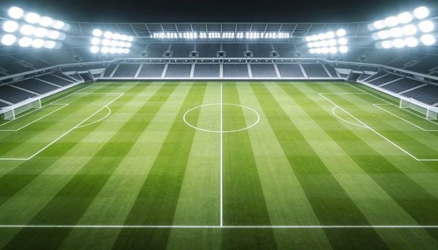Empty soccer stadium floodlit at night with striped pitch and aerial symmetry