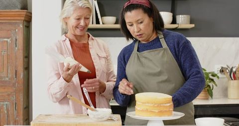 Senior women decorating cake together in home kitchen