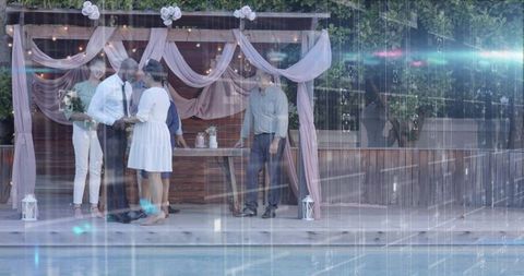 Couple exchanging vows under pink drapes at poolside pergola with lanterns and lights