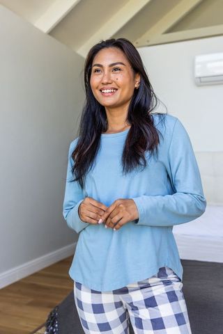 Young asian woman smiling in blue pajamas in cozy loft bedroom morning light