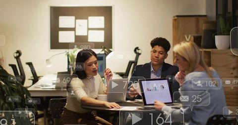Collaborative team reviewing laptop analytics dashboard with social media notification overlays
