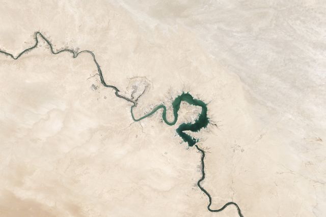 Aerial view of a winding river carving through a vast, arid desert landscape. The contrast between the lush green of the river and the surrounding barren terrain creates a striking natural pattern. Ideal for illustrating concepts related to geography, natural phenomena, environmental studies, and wilderness exploration. Useful for educational materials, travel guides, and conservation-related content.