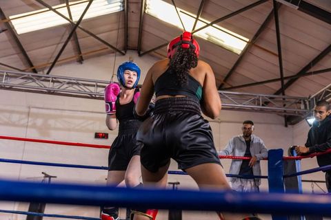 Female boxers sparring in gym ring wearing red and blue headgear and gloves