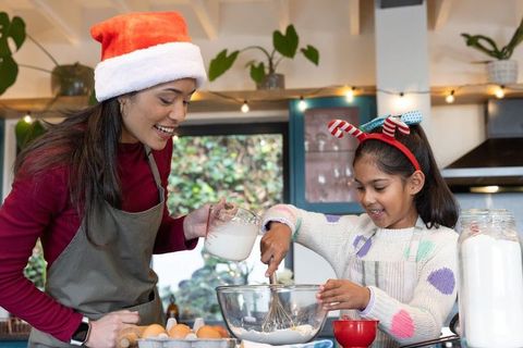 Indian mother and daughter baking holiday treats together in cozy home kitchen wearing festive hats