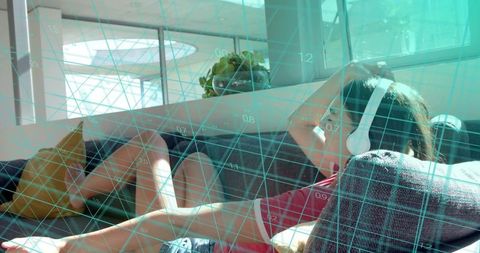 Reclining woman listening with white headphones on gray sofa amid teal grid overlay