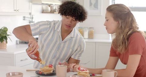 Couple sharing pancakes with syrup in cozy kitchen