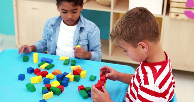 Two young Caucasian boys are engaged in play with colorful building blocks on a blue table, with copy space. Their focus and interaction with the educational toys suggest a learning environment that fosters creativity and cognitive development.