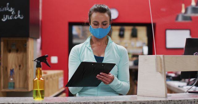 Female Gym Employee Wearing Mask Checking Documents at Reception Desk - Download Free Stock Images Pikwizard.com