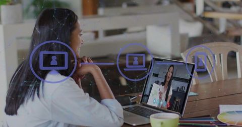 Woman joining video meeting on laptop at home workspace with creative tools and coffee
