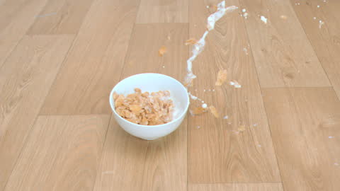 Bowl of Cereal Splattering Milk and Flakes on Floor
