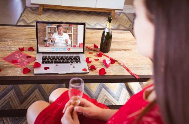 Caucasian mid adult man showing marry me text to girlfriend having champagne during online dating. unaltered, online dating, video call and distant valentine day celebration.