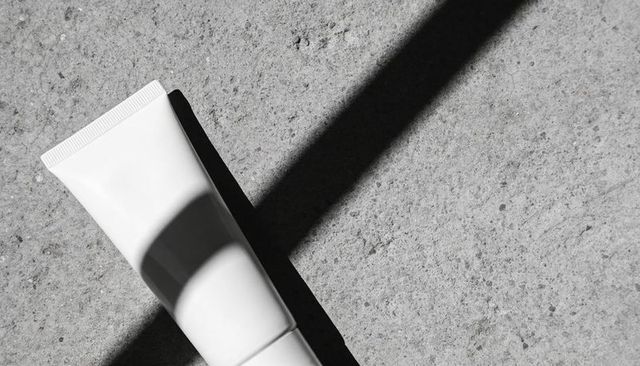 Minimalist skincare tube mockup casting bold diagonal shadow on rough concrete surface
