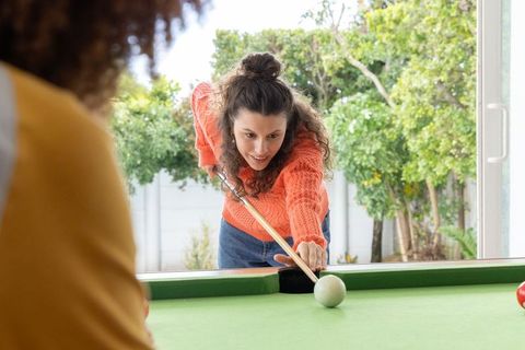 Friends playing pool in backyard game room woman aiming cue with focus and smile