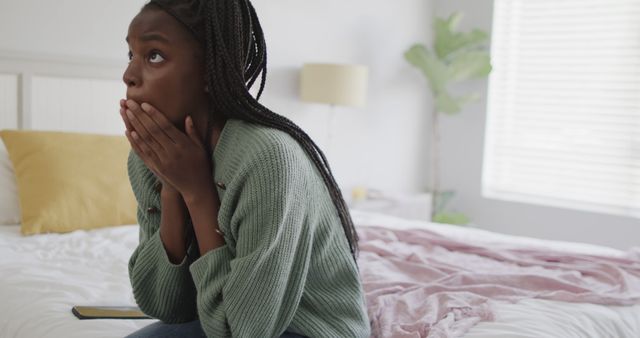 Sad african american teenage girl sitting on bed and covering her face. Mental health, emotion and lifestyle.