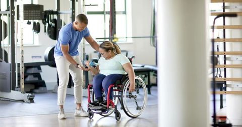 Trainer assisting woman in wheelchair lifting dumbbell during rehab workout
