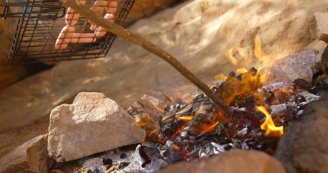 Hand Grilling Sausages over Campfire Flames in a Rocky Outdoor Setting - Download Free Stock Images Pikwizard.com