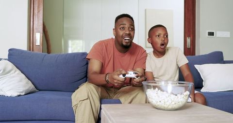 Father and son enjoying video game by blue couch with popcorn