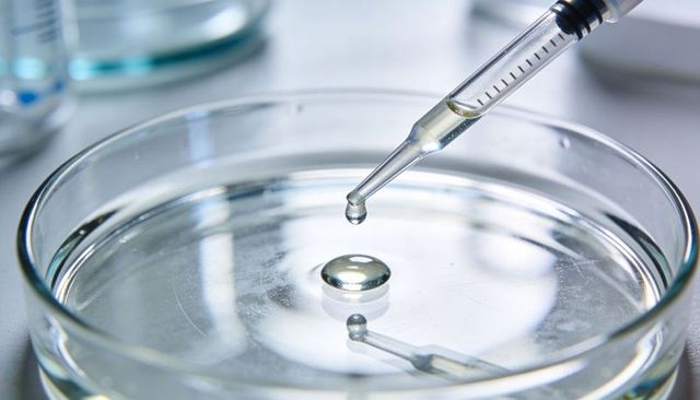 Pipette releasing droplet forming bead on petri dish with lab reflection and surface tension