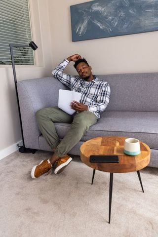 African american man sitting on sofa holding papers in minimalist living room calm