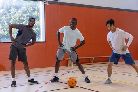 Diverse teammates stretching and warming up on indoor basketball court before practice