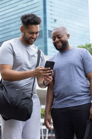 African american male friends checking smartphone by glass highrise urban lifestyle
