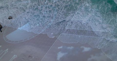Aerial surf meeting sandy shore with teal ocean and translucent digital overlay grid