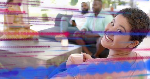 Smiling woman holding mug, chatting with friends, sunlit lounge with dotted color overlay