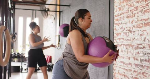 Women training with purple medicine balls during wall-ball strength workout in gym
