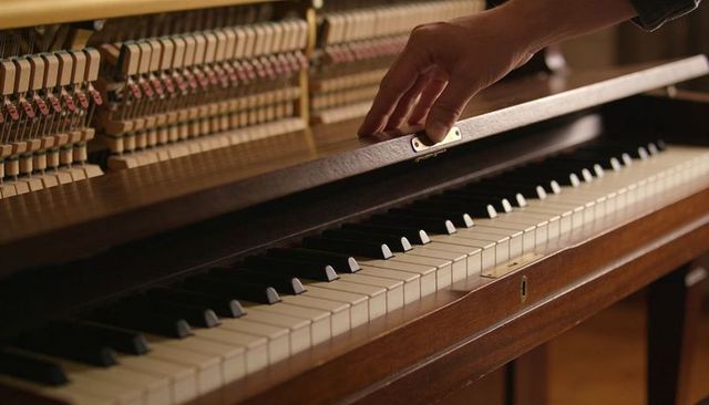 Hand lifting fallboard revealing hammers and ivory keys on vintage wooden upright piano