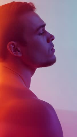 Vertical video male model raising head in gradient lighting showing profile and musculature
