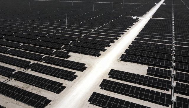 Aerial view of utility-scale solar farm stretching across arid land with access road