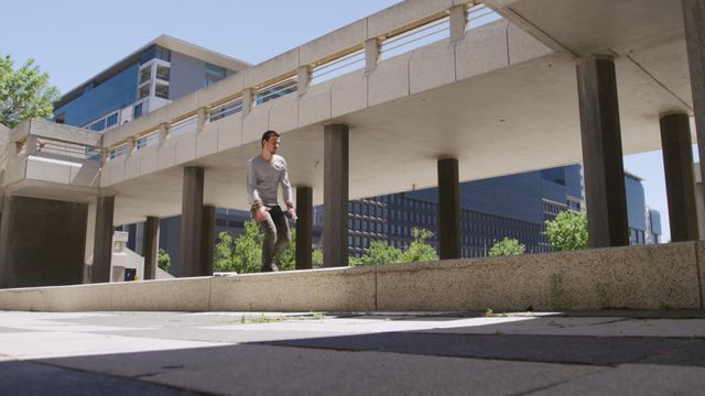 Dynamic scene showing man engaged in parkour moves amid city structures on a clear day, suggesting action, agility, and athleticism. Useful for articles about urban sports, fitness lifestyle, extreme sport advertising or motivational imagery celebrating determination and movement.