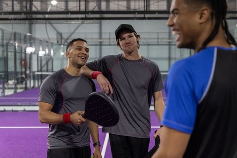 Multicultural men sharing laughs on indoor purple paddle court during casual team practice