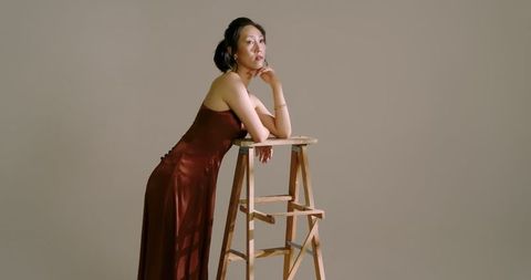 Elegant Woman in Brown Silk Dress Leaning on Stepladder