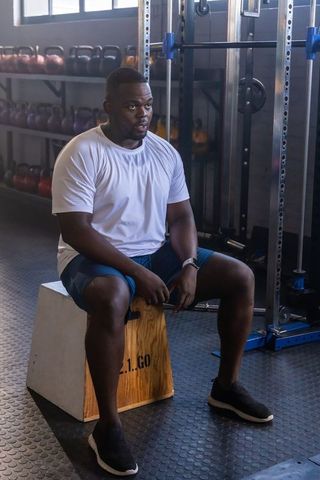 Male athlete resting on plyo box after intense strength training in modern gym