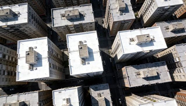 Aerial grid of midrise city blocks with white flat rooftops, hvac units and street shadows