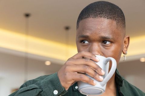 African american man drinking coffee from ribbed ceramic mug in warm interior, piercings
