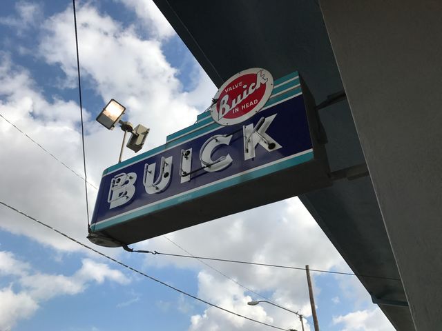 Classic Buick dealership sign with blue and white colors set against a partly cloudy sky. Ideal for automotive history enthusiasts, vintage car club promotions, and nostalgic branding projects.