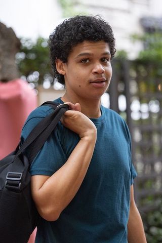 African american young man carrying backpack on urban sidewalk wearing teal t-shirt