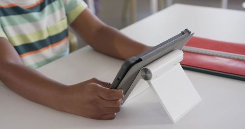 African american child using tablet on white stand learning at desk with notebooks and ruler