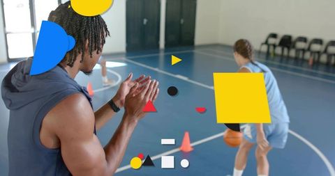 Coach clapping guiding player dribbling on blue indoor basketball court training session